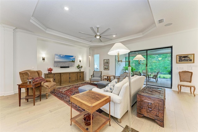 living room featuring ceiling fan, light wood-type flooring, crown molding, a tray ceiling, and baseboards