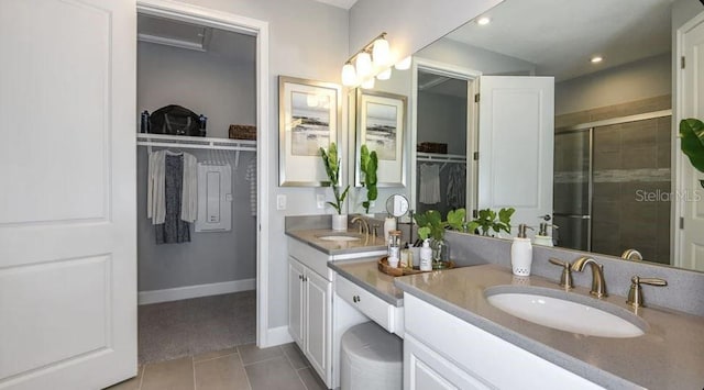 bathroom featuring a shower stall, tile patterned flooring, a walk in closet, double vanity, and baseboards