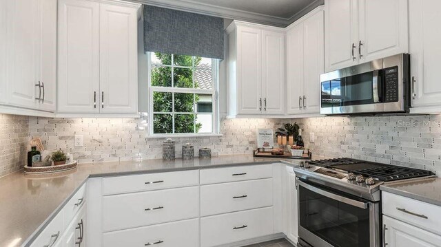 kitchen with stainless steel appliances, white cabinets, backsplash, and crown molding