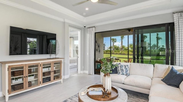 living room with ceiling fan, plenty of natural light, crown molding, a tray ceiling, and baseboards
