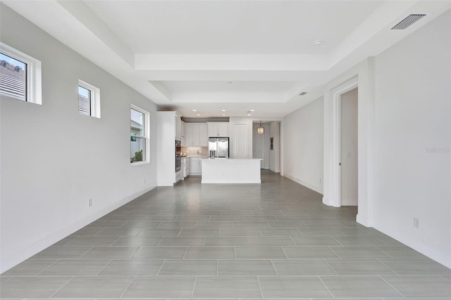 unfurnished living room with a raised ceiling, recessed lighting, and baseboards