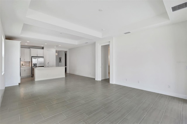 unfurnished living room with a raised ceiling, recessed lighting, baseboards, and a sink