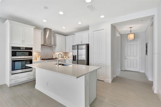 kitchen featuring appliances with stainless steel finishes, wall chimney range hood, a sink, light countertops, and white cabinets