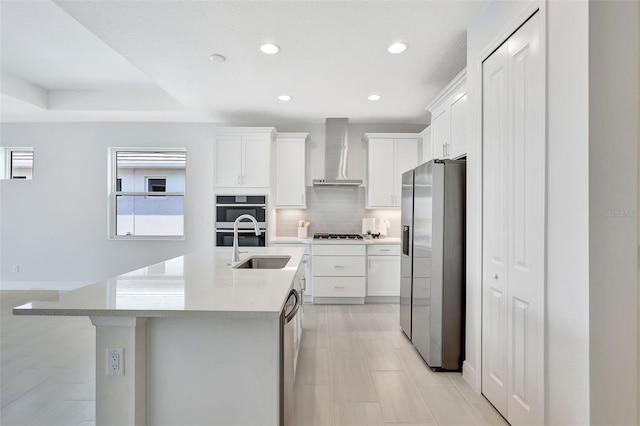 kitchen with appliances with stainless steel finishes, wall chimney exhaust hood, backsplash, a sink, and white cabinets