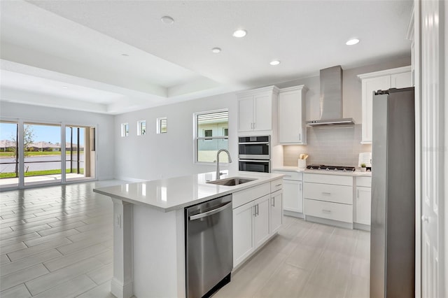 kitchen featuring stainless steel appliances, wall chimney range hood, a sink, tasteful backsplash, and light countertops