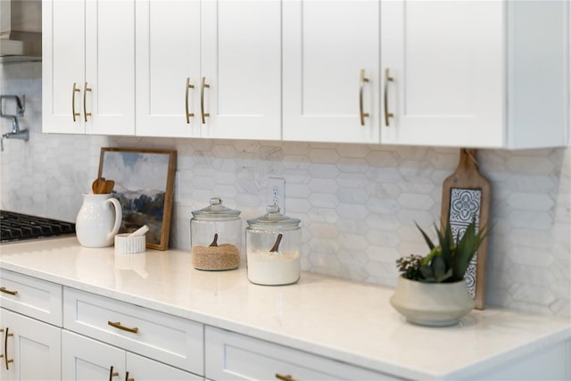 kitchen view of tasteful backsplash, extractor fan, white cabinetry, pot filler, and light stone countertops
