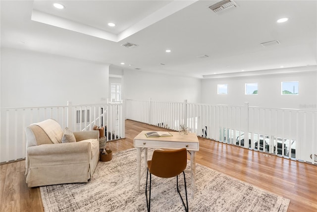 living area with recessed lighting, wood finished floors, healthy amount of natural light, an upstairs landing, and a tray ceiling