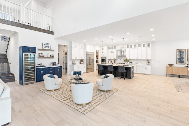 living area with wine cooler, stairway, recessed lighting, a towering ceiling, and light wood-style floors