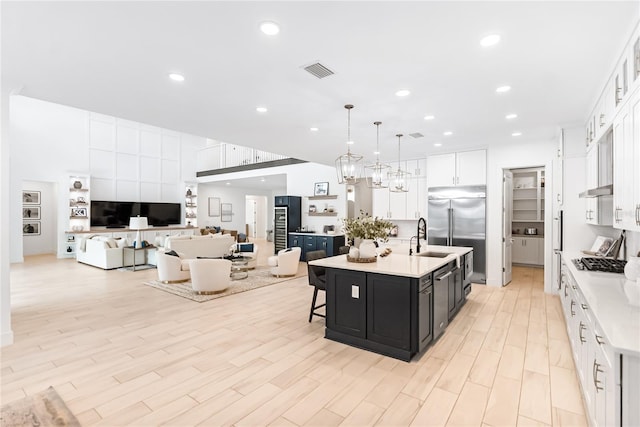 kitchen with dark cabinets, light countertops, appliances with stainless steel finishes, white cabinetry, and a center island with sink