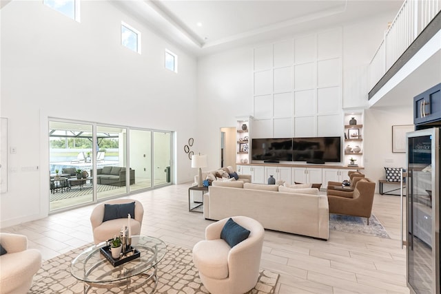 living area with a towering ceiling, plenty of natural light, a tray ceiling, light wood-style floors, and beverage cooler