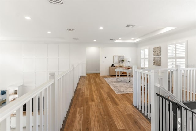hallway featuring an upstairs landing, wood finished floors, recessed lighting, and a raised ceiling