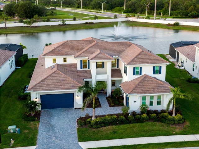 mediterranean / spanish house with a water view, a tile roof, decorative driveway, stucco siding, and a garage
