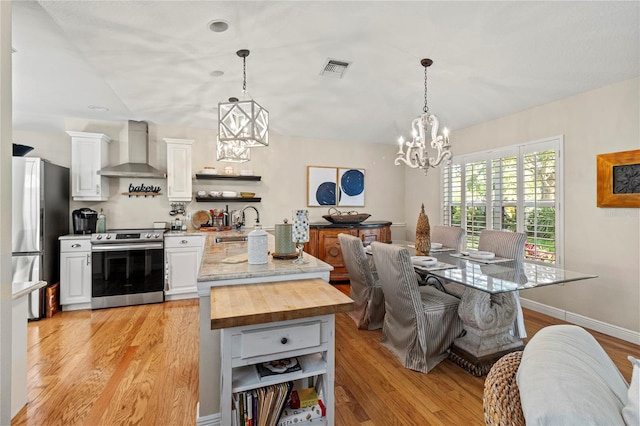 6402 23rd Avenue Dr W, Bradenton, FL 34209 - kitchen with appliances with stainless steel finishes, wall chimney exhaust hood, a chandelier, open shelves, and light wood finished floors