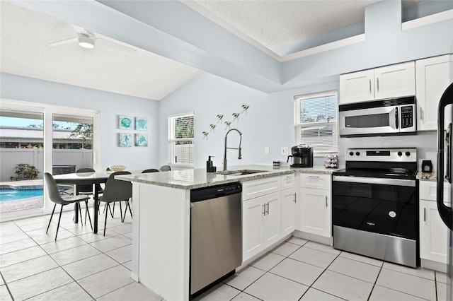 kitchen featuring appliances with stainless steel finishes, a sink, a textured ceiling, a peninsula, and light tile patterned floors