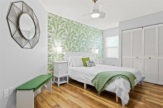 bedroom with wallpapered walls, a closet, an accent wall, a textured ceiling, and wood finished floors