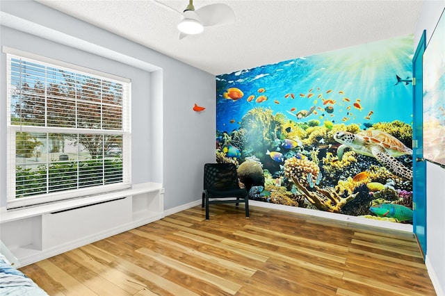 living area with wood finished floors, ceiling fan, a textured ceiling, and baseboards