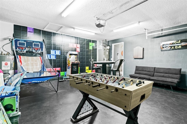 game room featuring concrete block wall, electric water heater, a textured ceiling, and concrete floors