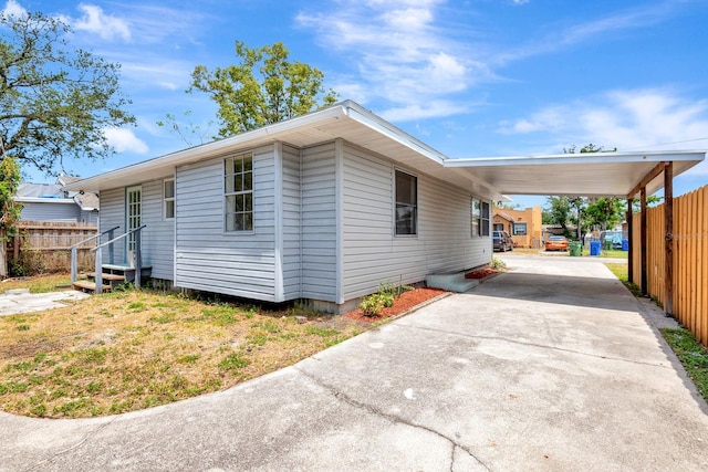 view of side of property featuring concrete driveway, fence, and an attached carport