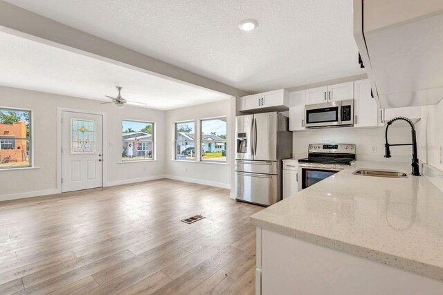 kitchen featuring appliances with stainless steel finishes, a sink, white cabinets, baseboards, and a textured ceiling