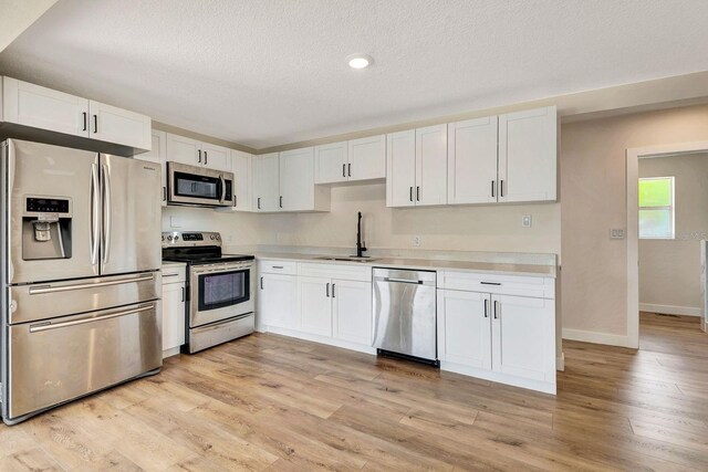 kitchen featuring stainless steel appliances, a sink, white cabinetry, light countertops, and a textured ceiling