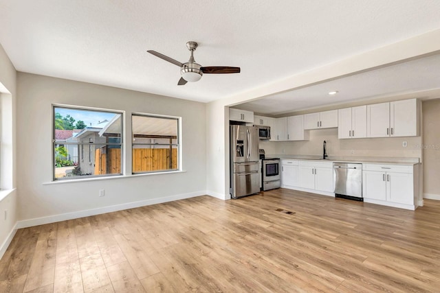 kitchen with stainless steel appliances, light countertops, light wood-style flooring, ceiling fan, and baseboards