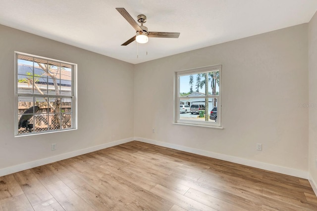 empty room with healthy amount of natural light, wood finished floors, a ceiling fan, and baseboards