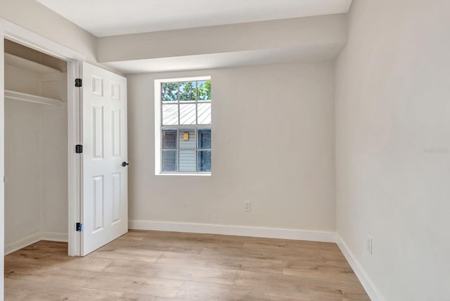 unfurnished bedroom featuring light wood-type flooring, baseboards, and a closet