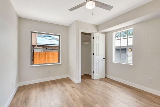 unfurnished bedroom featuring light wood-style flooring, baseboards, a walk in closet, and ceiling fan