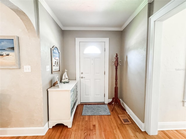 foyer entrance featuring light wood-style flooring, arched walkways, baseboards, and ornamental molding