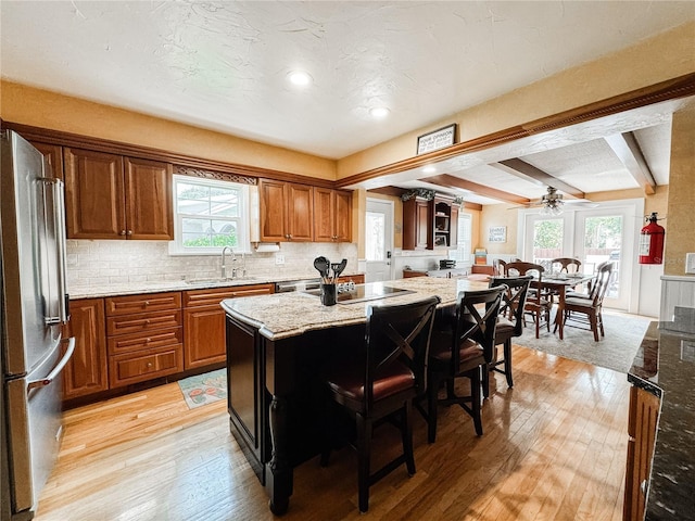 kitchen with freestanding refrigerator, light wood finished floors, brown cabinetry, a center island, and beam ceiling