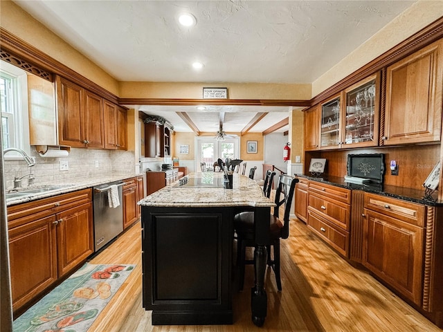 kitchen with stainless steel dishwasher, a sink, a kitchen island, light wood-style floors, and brown cabinets