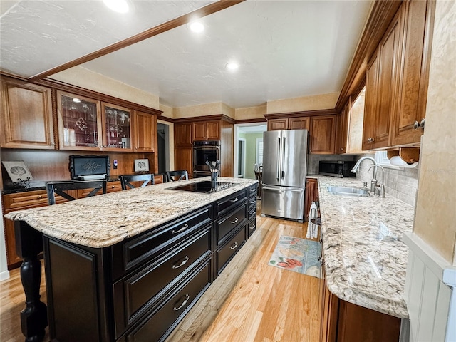 kitchen with stainless steel appliances, a sink, an island with sink, light wood-style flooring, and light stone counters