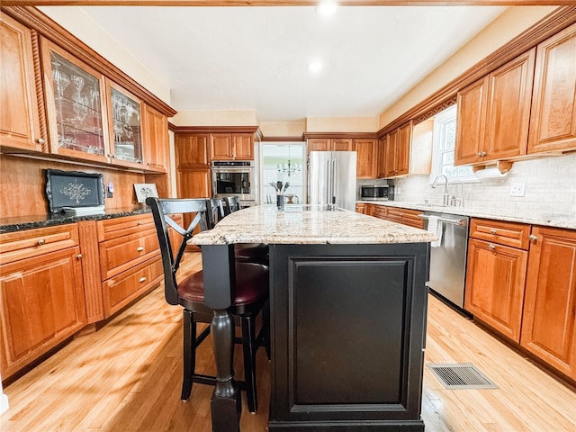 kitchen with appliances with stainless steel finishes, light wood-style flooring, a sink, a breakfast bar area, and a kitchen island