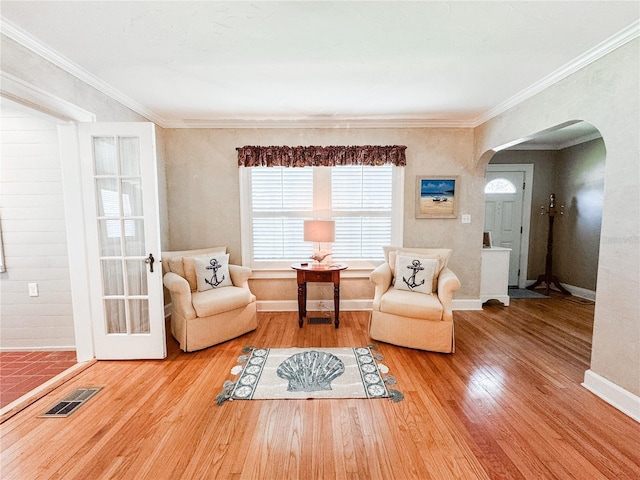 sitting room with arched walkways, wood finished floors, crown molding, and baseboards