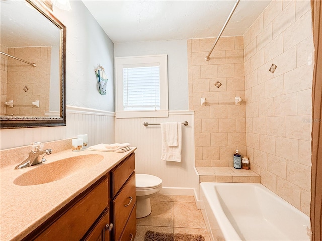bathroom featuring toilet, tile patterned flooring, vanity, washtub / shower combination, and wainscoting
