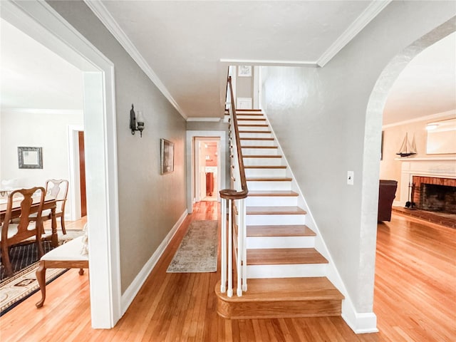 staircase with wood-type flooring, crown molding, a fireplace, arched walkways, and baseboards
