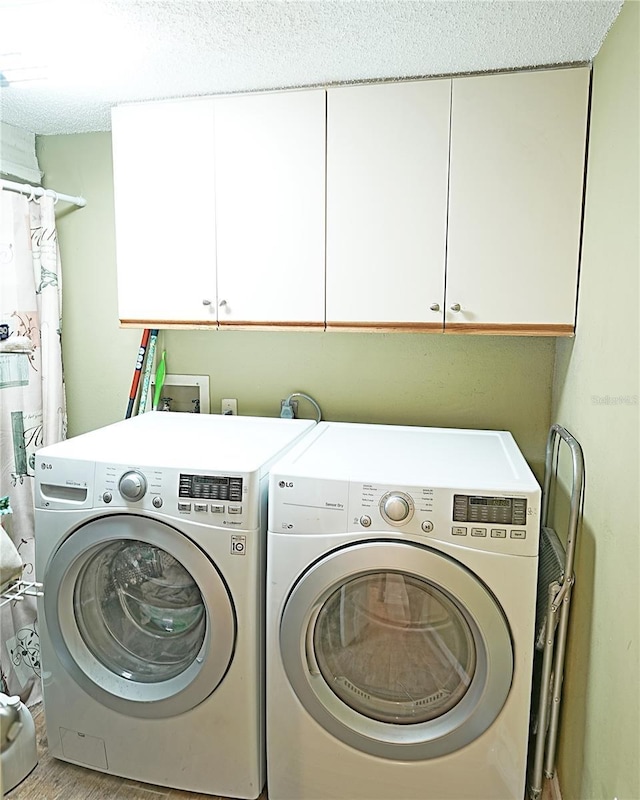 clothes washing area with cabinet space, washer and clothes dryer, and a textured ceiling