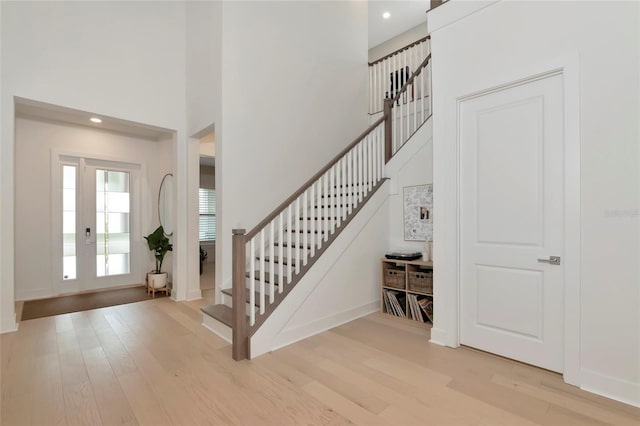 foyer entrance with stairs, light wood finished floors, a high ceiling, recessed lighting, and baseboards