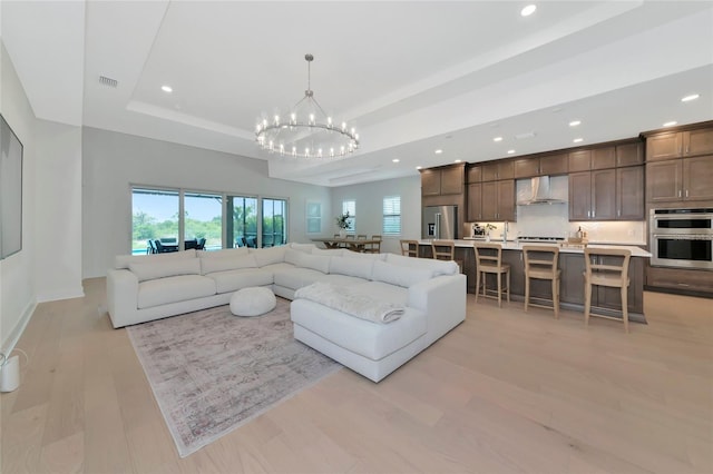 living area featuring a chandelier, recessed lighting, a tray ceiling, light wood-type flooring, and baseboards