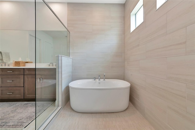 bathroom with tile walls, a freestanding bath, vanity, and a tile shower