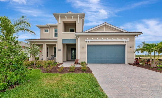 view of front of home featuring decorative driveway, an attached garage, stucco siding, covered porch, and a front yard