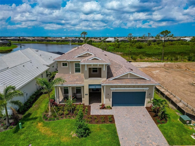view of front of property with decorative driveway, a water view, a garage, stucco siding, and a tiled roof