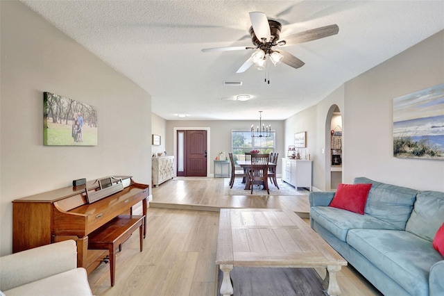 living room featuring arched walkways, ceiling fan, a chandelier, light wood-style flooring, and baseboards