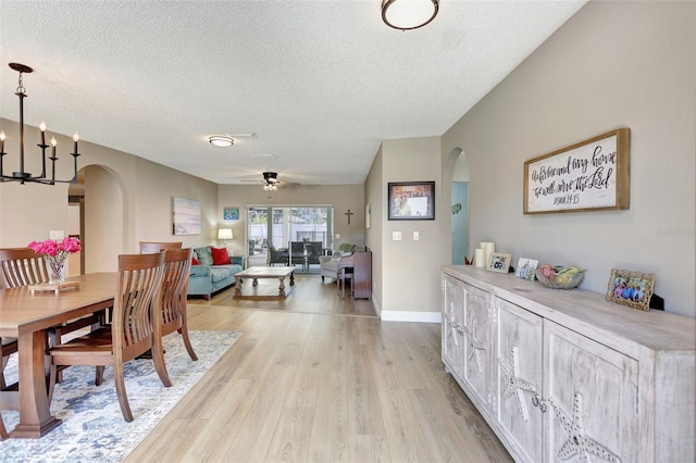 dining room featuring arched walkways, a textured ceiling, light wood finished floors, ceiling fan, and a chandelier