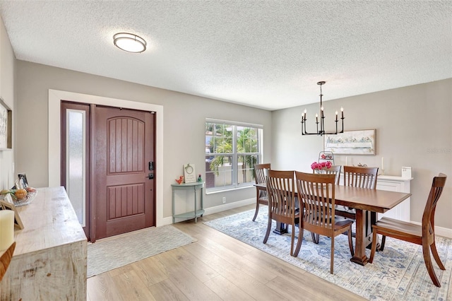 dining area featuring a chandelier, light wood-style flooring, a textured ceiling, and baseboards