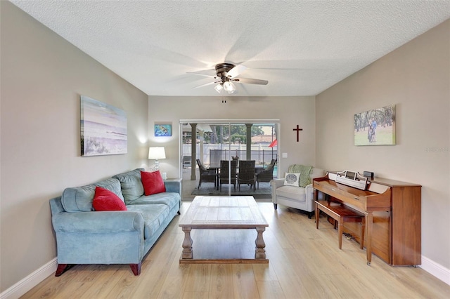 living area with a ceiling fan, light wood finished floors, a textured ceiling, and baseboards