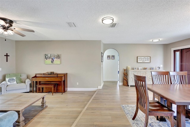dining area featuring arched walkways, a ceiling fan, light wood-style flooring, a textured ceiling, and baseboards