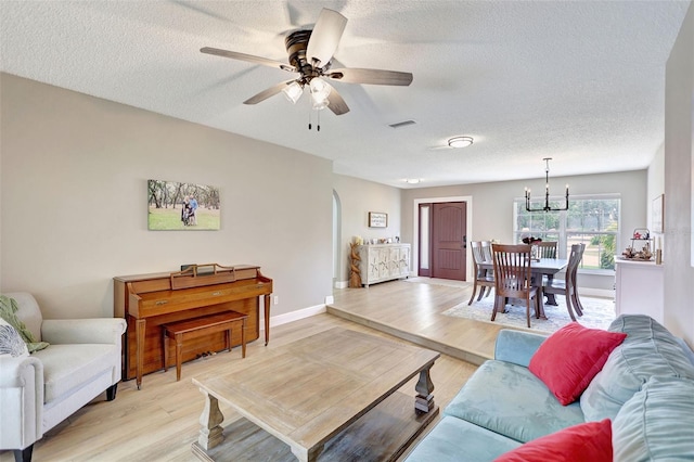 living area featuring light wood-style floors, a textured ceiling, a chandelier, ceiling fan, and baseboards