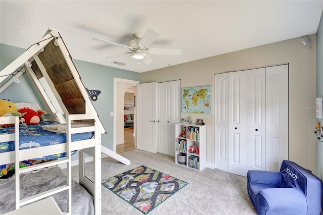 carpeted bedroom with multiple closets, a ceiling fan, baseboards, a textured ceiling, and arched walkways