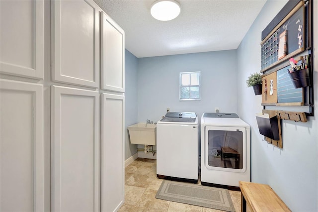 washroom with washing machine and clothes dryer, cabinet space, a textured ceiling, and baseboards